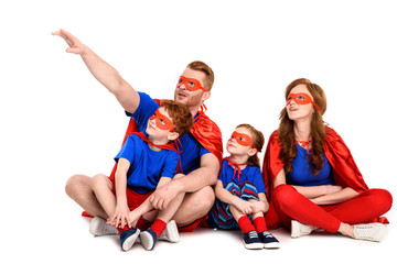 super family in costumes sitting together and looking away isolated on white
