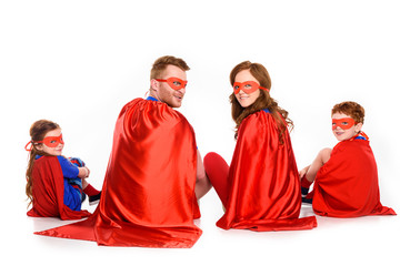 back view of family of superheroes sitting together and looking at camera isolated on white