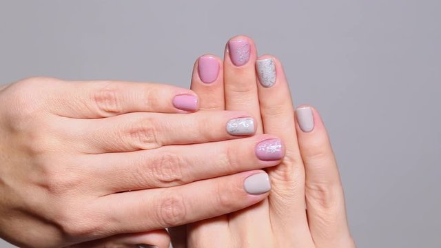 Closeup view of two female white hands with modern beautiful grey and pink manicure on small fingernails made with gel polish.