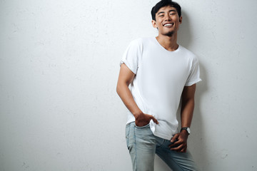 Smiling asian man in white blank t-shirt, grunge wall, studio portrait