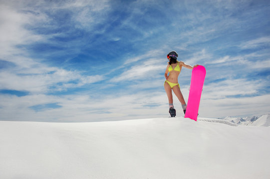 Sexy woman in swimsuit and helmet with a snowboard on the mountain slope