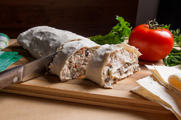 Pieces of cutted pita bread or lavash roll with cottage cheese or curd, chicken, tomatoes and herbs - dill, onion, parsley with intige knife on cutting board..