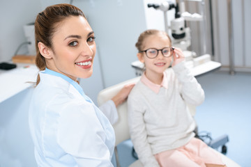 smiling ophthalmologist and kid in eyeglasses in optics