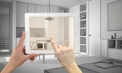 Hands holding and pointing on tablet showing real finished minimalist white kitchen. Modern kitchen CAD sketch in the background, architecture interior design presentation