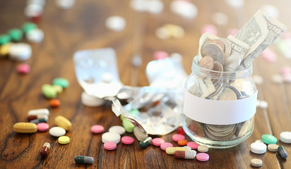 Fototapeta na wymiar Drugs and coins in a glass jar on a wooden floor. Pocket savings
