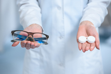 cropped view of ophthalmologist holding eyeglasses and and contact lenses in hands - obrazy, fototapety, plakaty