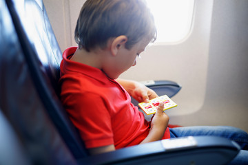 Little kid boy playing tic tac toe game during flight on airplane.