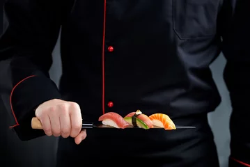 Tuinposter Sushi served on japanese knife in chef hand © nioloxs