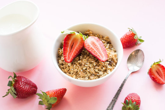Healthy breakfast of granola, strawberry and milk on pink. Summer.
