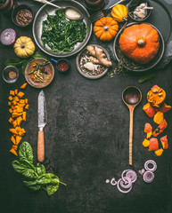 Autumn seasonal food, eating and cooking background with pumpkin.  Dark rustic kitchen table  with tools, bowls, spoons, knife, whole pumpkin and vegetables, top view, frame. Vegetarian food