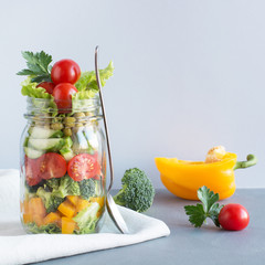 Vegetable healthy homemade colorful salad in mason jar with tomato, lettuce, yellow papper on blue. Copy space. Lunch for work. Food set.