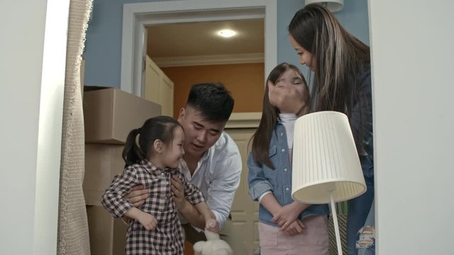 Medium shot of happy Asian family with children chatting and looking at interior of new house after moving