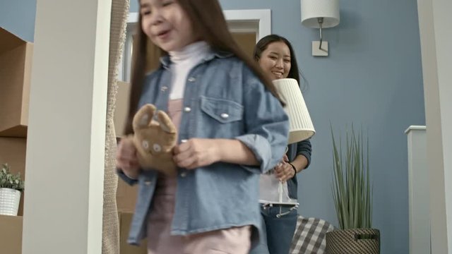 Medium shot of excited little girls with plush toys running into living room of new house as their parents hugging and smiling after unloading belongings