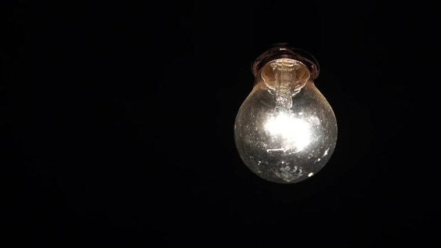 included light bulb slowly swings on the wire. the incandescent lamp is shining in the dark. Slow motion
