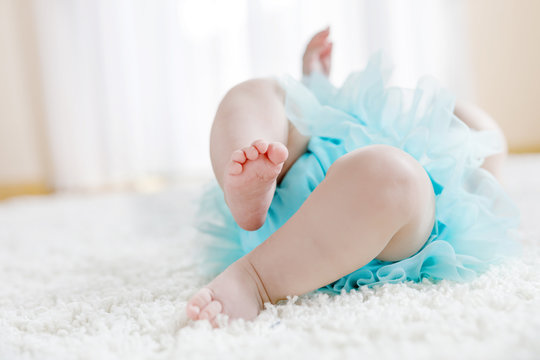Close up of legs and feet of baby girl on white background wearing turquoise tutu skirt.