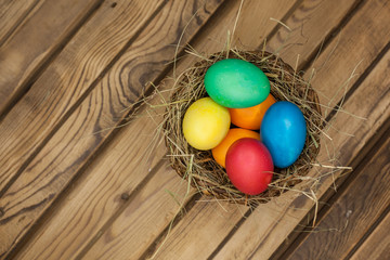 Easter eggs of different colors in a wicker basket with hay top view