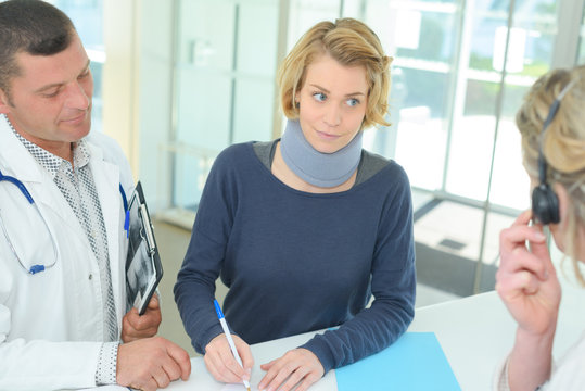 female patient with cervical collar in clinic signing document