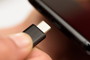 Persons hand inserting a USB cable charger into a mobile phone