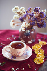 The vase with flowers, cup of tea  and pieces of mandarins  stand on the table