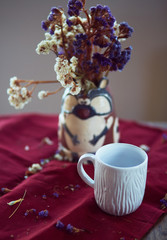 The vase with flowers and cup stand on the table