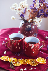 The vase with flowers, cups of tea  and pieces of mandarins  stand on the table