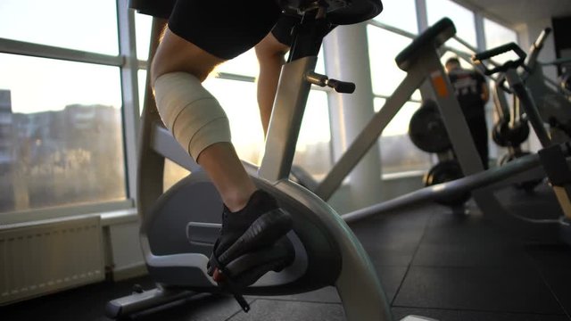 Athlete male with bandaged leg riding stationary bike in morning, recovery