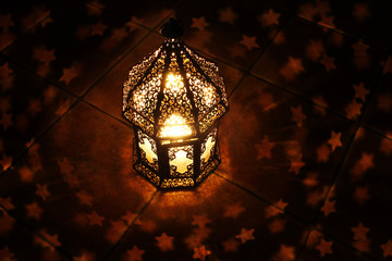 Ornamental Arabic lantern with burning candle glowing at night and glittering stars shaped bokeh...