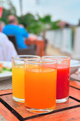 Three glasses with freshly squeezed juices: tomato, mango, orange stands on an vintage wooden table.