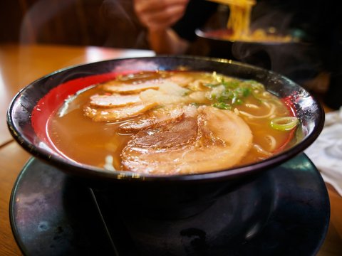 Wide close-up detail of a bowl of hot miso ramen topped with roasted chashu pork with customers eating in the background.  Osaka, Japan. Travel and cuisine concept.