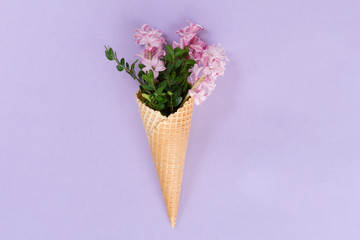 View from above of waffle cone with flower composition on lilac background with copy space, flat lay