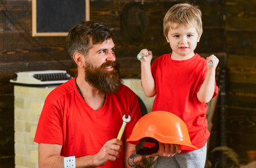 Safety and protection concept. Boy, child cheerful holds bolts or screws, having fun while handcrafting with dad. Father, parent with beard holds helmet teaching son safety in school workshop.