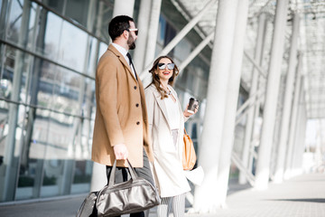 Business couple in coats walking out the airport with luggage during the business trip