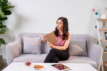 Happy pretty cute woman writing in the copybook sitting with laptop in living room