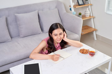 Beautiful woman at home writing and working with diary and digital tablet.