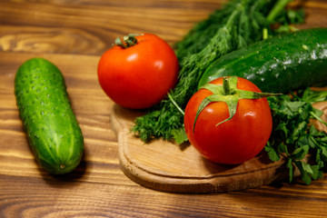 Fresh tomatoes, cucumbers, parsley and dill on cutting board on wooden table