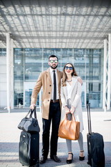 Business couple in coats standing near the airport with luggage during the business trip