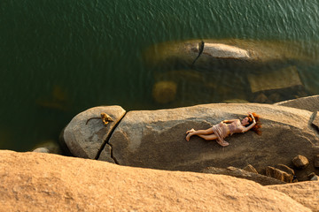 Young woman relaxes on the rocky shore of a beautiful lake. Her their body is framed by a rock. The...