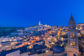 panoramic view of typical stones Sassi di Matera and church of Matera under blue night sky. Basilicata, Italy with clouds movement in the sky