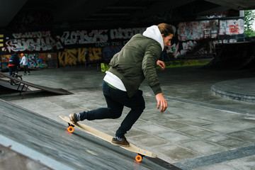 Fototapeta premium Longboarding in motion. Handsome young man longboarding and looking away with smile in skateboard park outdoors 