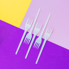 Plastic forks on geometric purple, pink and yellow background of paper textures. Minimal flat lay