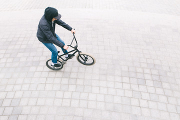 A young man in casual clothing, riding a bike on the rear wheel of a BMX. The minimalist photo of the BMX cyclist is from above. bmx culture