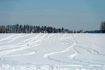 Fototapeta na wymiar Drawings from snowmobile tracks on a snow-covered field in a winter day