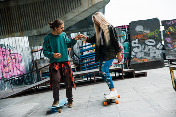 I can teach you. Young handsome men teaching his girlfriend how to ride longboard in skateboard...