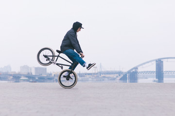 Young BMX bicycle rider rides on the front wheel against the background of the minimalistic urban landscape.BMX concept.