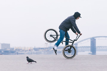 A young man in a casual clothing rides on a bmx bike front wheel. Stunts on bmx