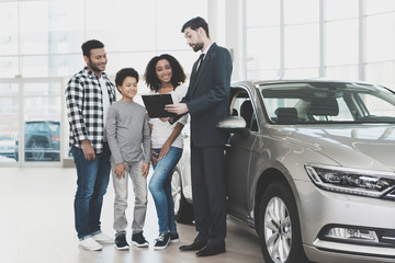 African american family at car dealership. Salesman is signing papers for new car.