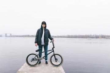 Portrait of a BMX rider standing with a bike on the background of the river. Walking with BMX by...
