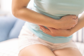Young woman suffering from abdominal pain while sitting on the sofa and feeling stomachache,...