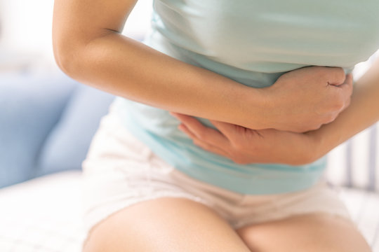 Young woman suffering from abdominal pain while sitting on the sofa and feeling stomachache, symptom of pms