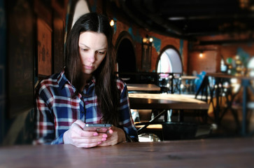 Upset woman sends a message in the phone sitting in a cafe. Dressed in a plaid shirt.
